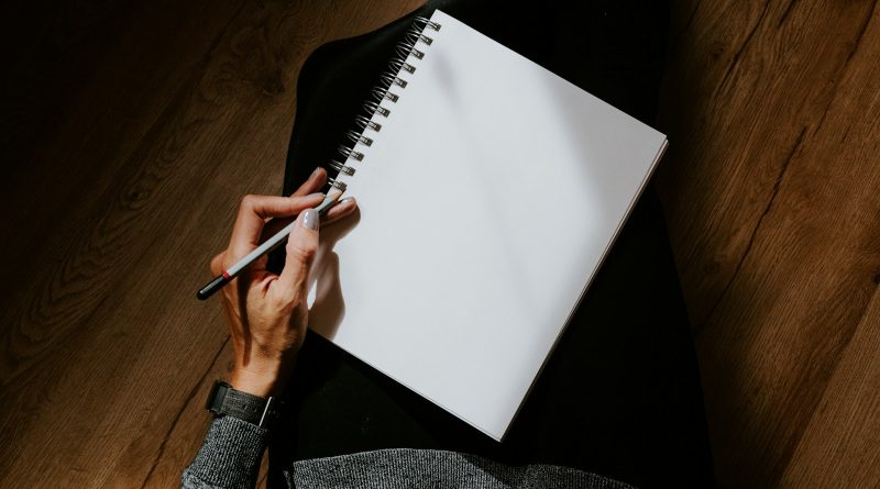 Learning after work: a hand holding a pencil, about to write in a spiral notebook
